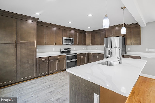 kitchen featuring pendant lighting, sink, appliances with stainless steel finishes, light stone counters, and an island with sink