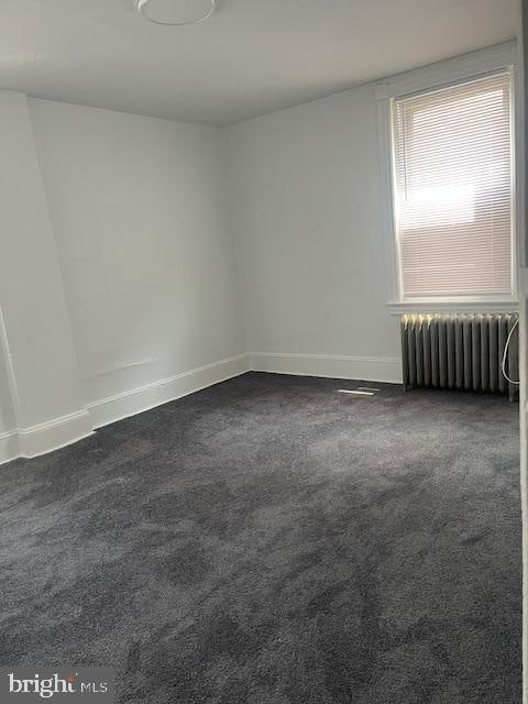 unfurnished room featuring radiator and dark colored carpet