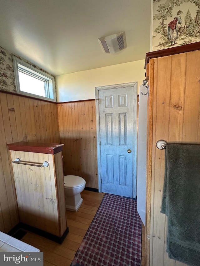 bathroom with wood-type flooring, wooden walls, and toilet