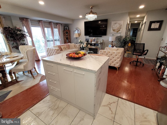 kitchen with white cabinets, light wood-type flooring, a kitchen island, and light stone countertops