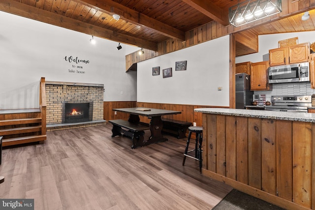 kitchen with a kitchen breakfast bar, light wood-type flooring, a brick fireplace, wood ceiling, and stainless steel appliances