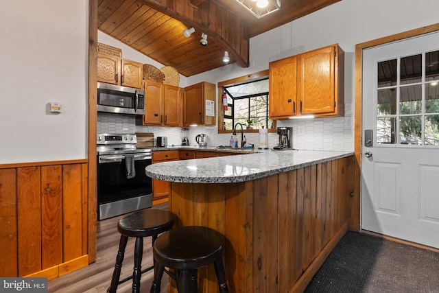 kitchen featuring wooden ceiling, a kitchen breakfast bar, kitchen peninsula, vaulted ceiling, and appliances with stainless steel finishes