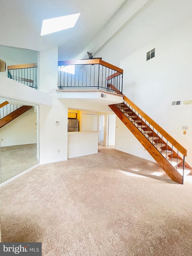 unfurnished living room with carpet, high vaulted ceiling, a skylight, ceiling fan, and beam ceiling