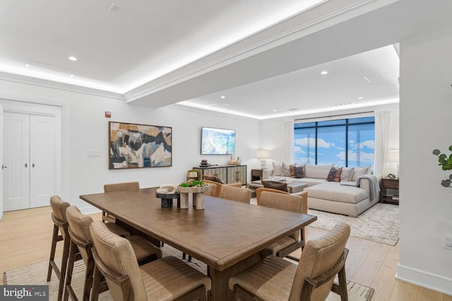 dining area featuring a raised ceiling, ornamental molding, and light hardwood / wood-style flooring