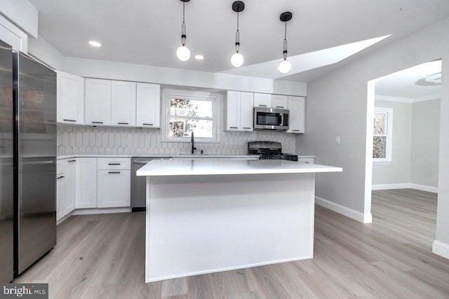 kitchen with a kitchen island, stainless steel appliances, pendant lighting, light wood-type flooring, and white cabinets