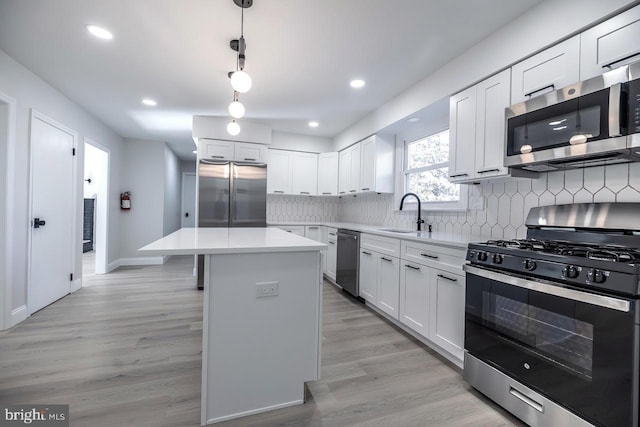 kitchen featuring light wood-type flooring, a center island, hanging light fixtures, stainless steel appliances, and white cabinets