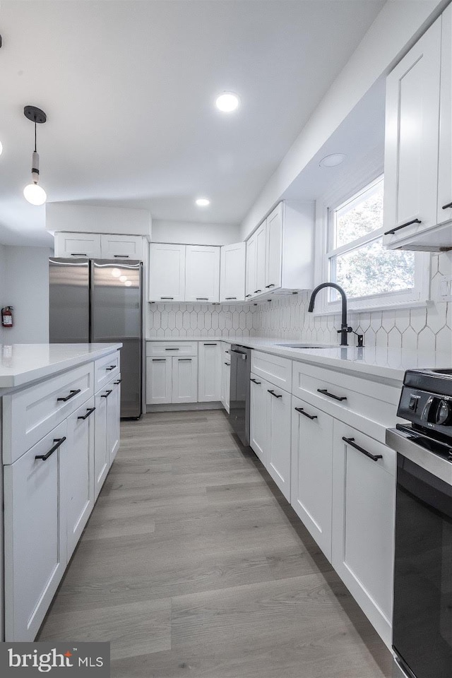 kitchen featuring appliances with stainless steel finishes, sink, light wood-type flooring, hanging light fixtures, and white cabinetry