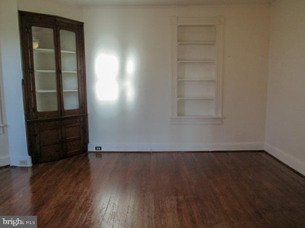 spare room featuring built in features and dark hardwood / wood-style floors