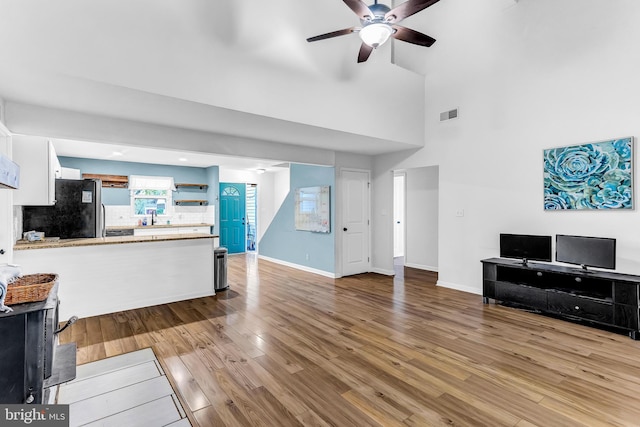 living room featuring ceiling fan, a towering ceiling, and light hardwood / wood-style flooring