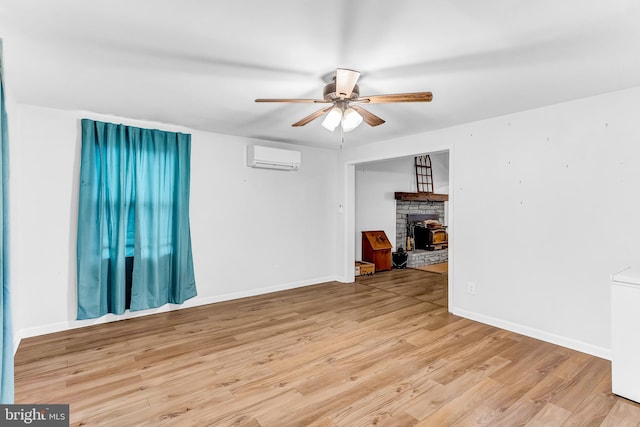 empty room with ceiling fan, light wood-type flooring, a fireplace, and a wall unit AC