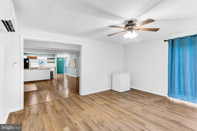 unfurnished room with a wall mounted AC, ceiling fan, and light hardwood / wood-style floors