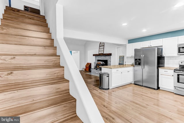 kitchen featuring white cabinets, backsplash, stainless steel appliances, and light hardwood / wood-style flooring