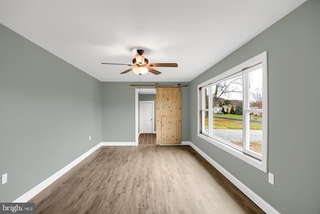 unfurnished bedroom with hardwood / wood-style flooring, ceiling fan, and a barn door