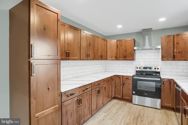 kitchen featuring appliances with stainless steel finishes, backsplash, light stone counters, wall chimney exhaust hood, and light hardwood / wood-style flooring