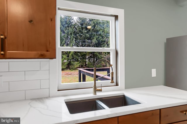 kitchen featuring backsplash, light stone countertops, sink, and a healthy amount of sunlight