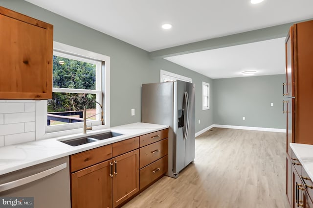 kitchen with appliances with stainless steel finishes, backsplash, light stone counters, sink, and light hardwood / wood-style flooring