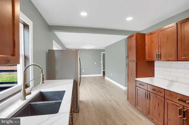 kitchen with sink, light wood-type flooring, tasteful backsplash, light stone counters, and stainless steel refrigerator