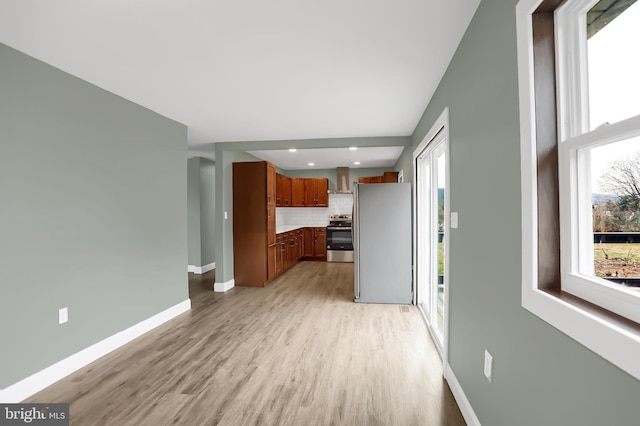 kitchen featuring backsplash, light hardwood / wood-style floors, wall chimney range hood, and stainless steel appliances