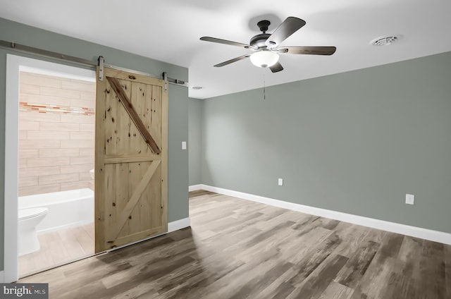 unfurnished room featuring ceiling fan, a barn door, and wood-type flooring