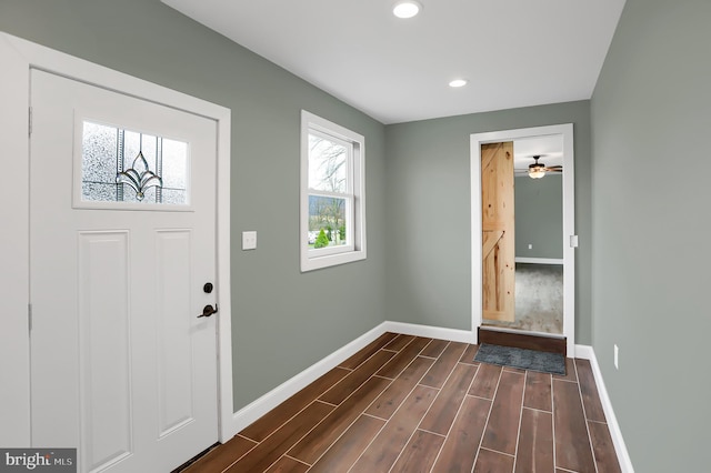 foyer entrance featuring ceiling fan, a barn door, and dark hardwood / wood-style flooring