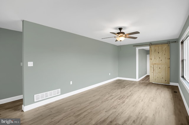 unfurnished bedroom featuring a barn door, ceiling fan, and wood-type flooring