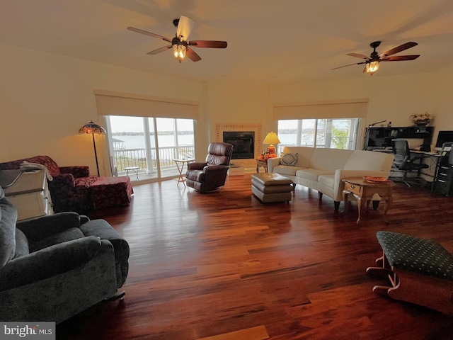 living room featuring ceiling fan, a tiled fireplace, dark hardwood / wood-style flooring, and a healthy amount of sunlight