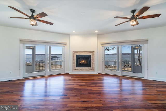 unfurnished living room featuring ceiling fan, a water view, and dark hardwood / wood-style flooring