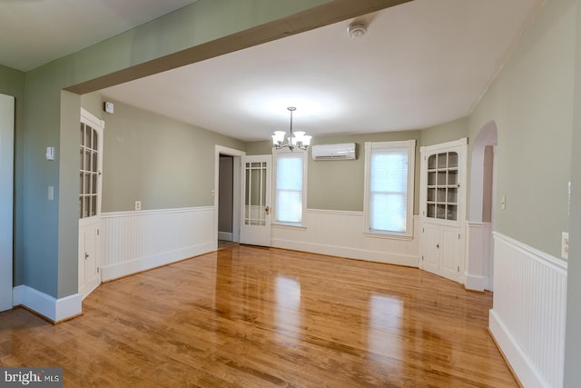 unfurnished dining area featuring a wall mounted AC, light hardwood / wood-style flooring, and an inviting chandelier