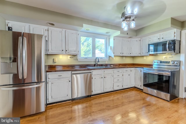 kitchen featuring appliances with stainless steel finishes, sink, ceiling fan, white cabinets, and light hardwood / wood-style flooring