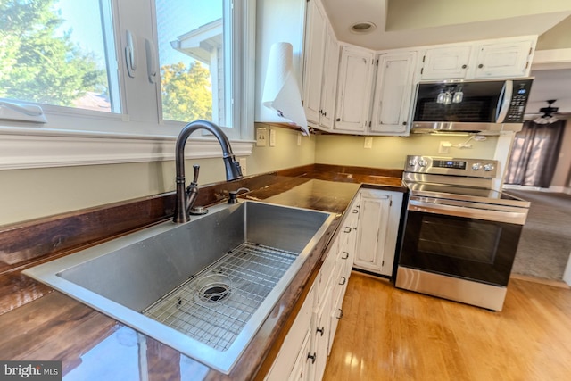 kitchen with sink, white cabinetry, appliances with stainless steel finishes, light hardwood / wood-style floors, and ceiling fan