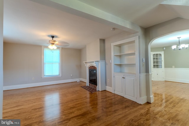 unfurnished living room featuring light hardwood / wood-style flooring, ceiling fan with notable chandelier, and built in shelves