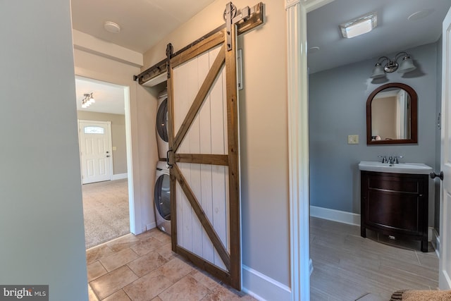 hallway with sink, stacked washer and dryer, light colored carpet, and a barn door