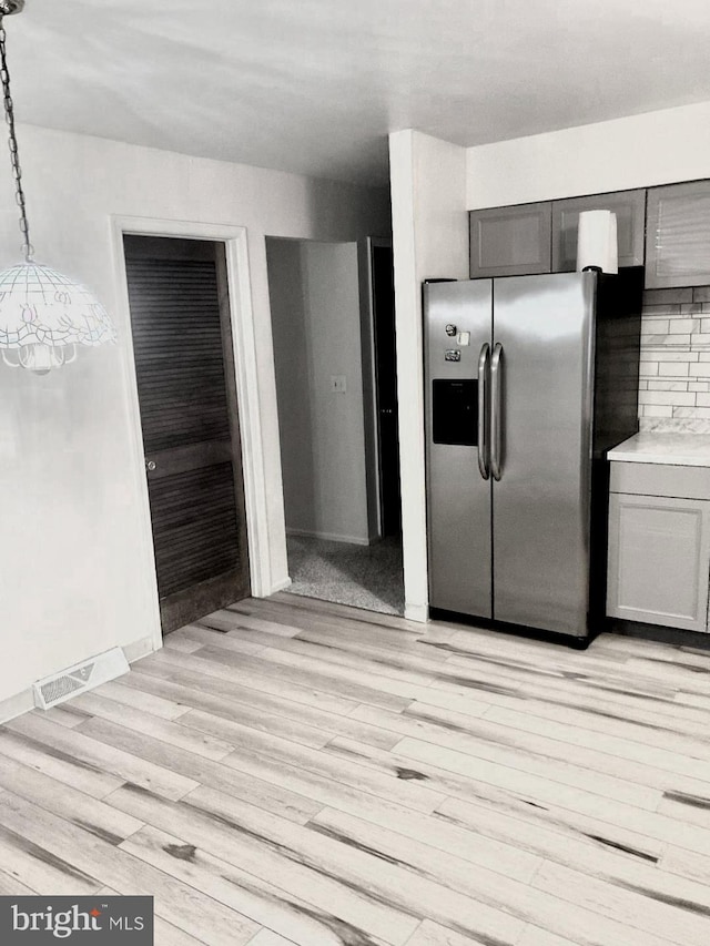 kitchen with light hardwood / wood-style floors, stainless steel fridge, tasteful backsplash, and pendant lighting