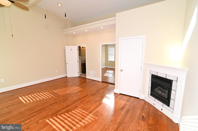 unfurnished living room with high vaulted ceiling, hardwood / wood-style floors, a tile fireplace, and ceiling fan