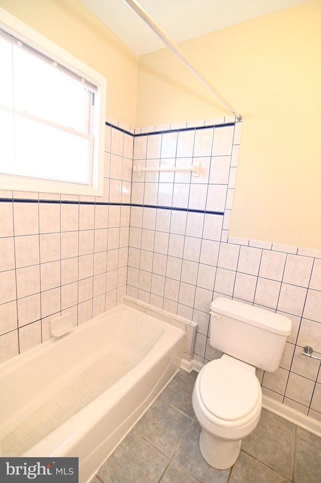 bathroom with tile walls, tile patterned flooring, tiled shower / bath, and toilet