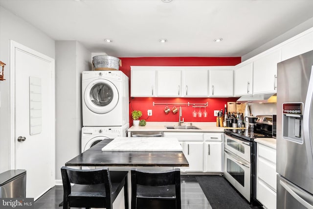 kitchen featuring stacked washing maching and dryer, stainless steel appliances, dark hardwood / wood-style flooring, sink, and white cabinets