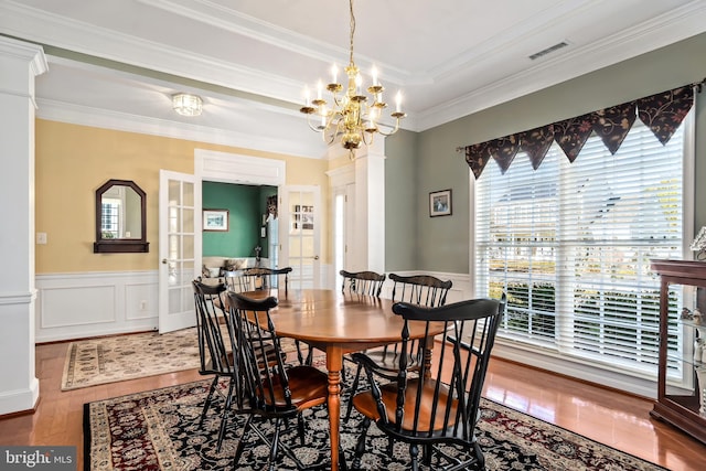 dining area with wood-type flooring, ornate columns, an inviting chandelier, and crown molding