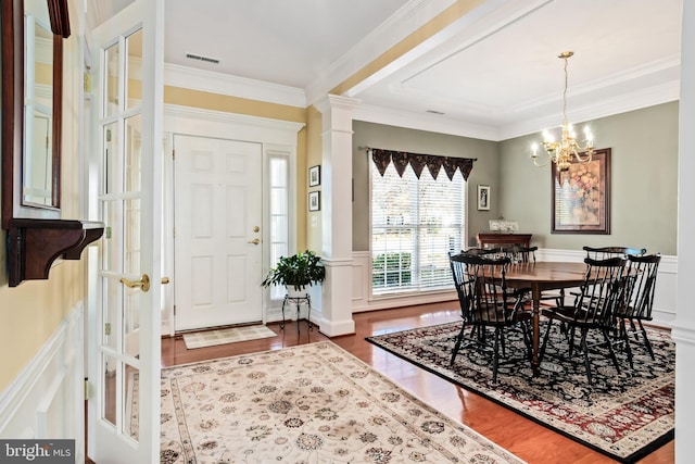 dining space featuring dark wood-type flooring, a notable chandelier, ornate columns, and ornamental molding