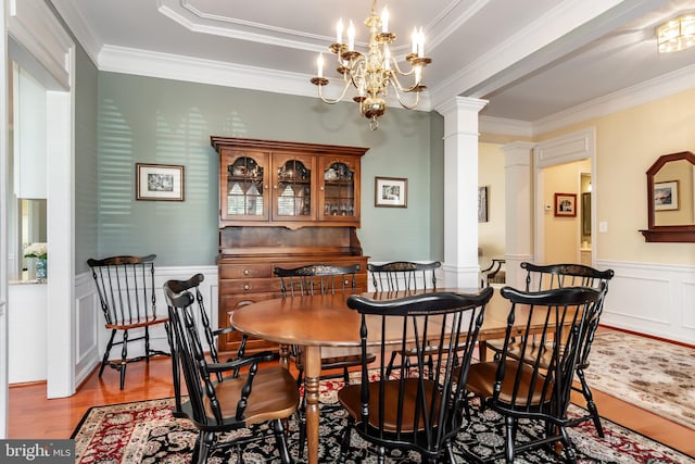 dining room with ornate columns, light hardwood / wood-style flooring, crown molding, and a notable chandelier