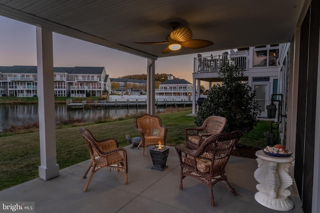 patio terrace at dusk with a lawn, a water view, and ceiling fan