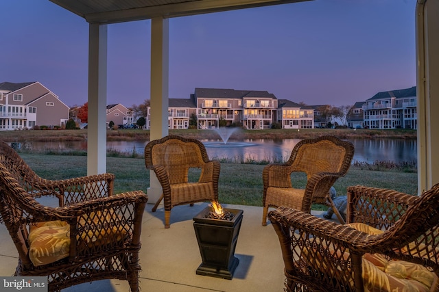 patio terrace at dusk featuring a water view and a lawn