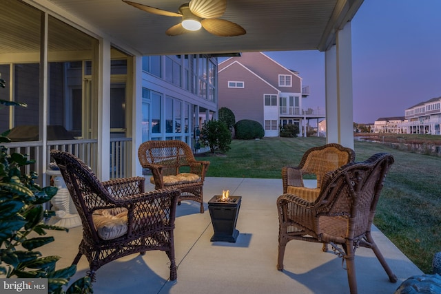 patio terrace at dusk with ceiling fan, a lawn, and a fire pit