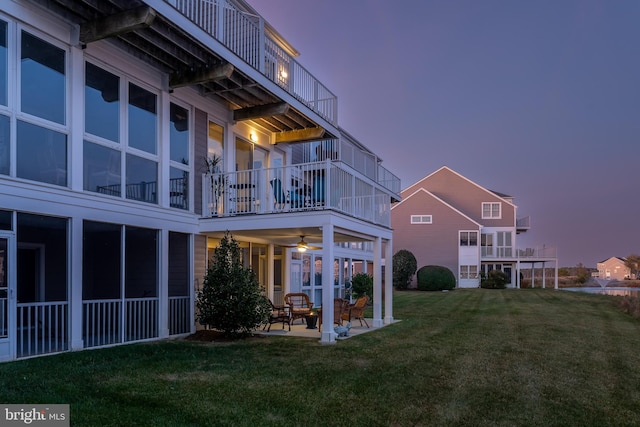 back house at dusk with a patio, a balcony, a lawn, and ceiling fan