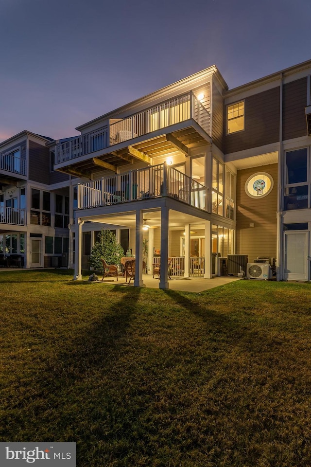 back house at dusk featuring central air condition unit, a patio area, a yard, and a balcony