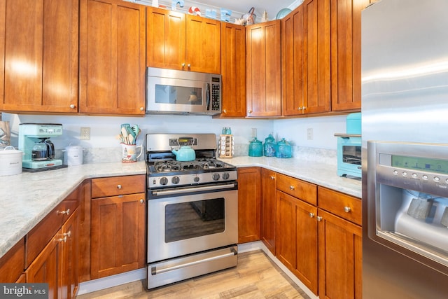 kitchen with appliances with stainless steel finishes, light hardwood / wood-style flooring, and light stone countertops