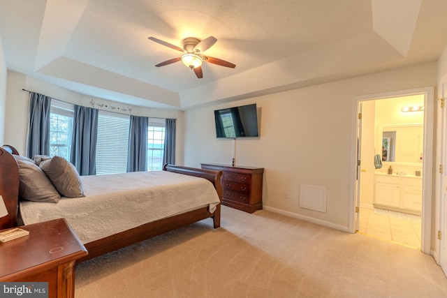 carpeted bedroom with a tray ceiling, ceiling fan, and ensuite bathroom