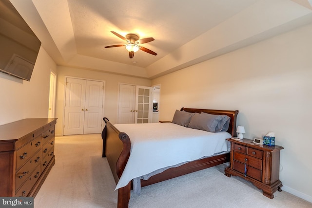 carpeted bedroom with a tray ceiling, two closets, and ceiling fan