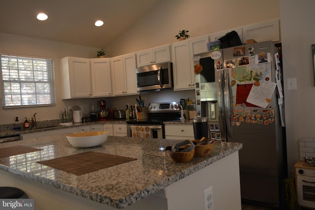 kitchen with stainless steel appliances, vaulted ceiling, a center island, white cabinetry, and light stone counters