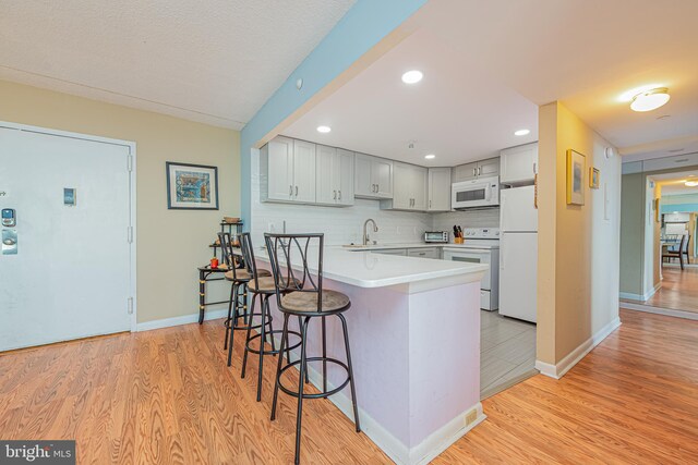 kitchen with a breakfast bar area, tasteful backsplash, light wood-type flooring, and white appliances