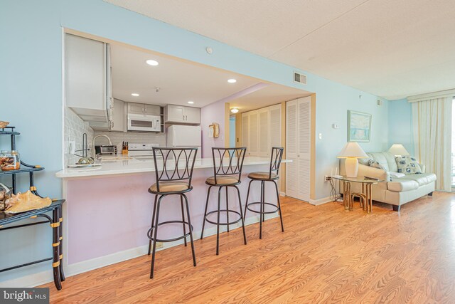 kitchen featuring kitchen peninsula, a breakfast bar area, white cabinetry, light wood-type flooring, and white appliances